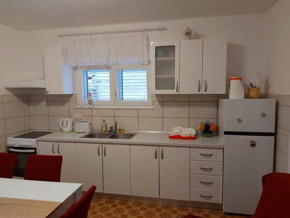 Cocina compacta con armarios blancos, un lavamanos, una estufa y un refrigerador.
