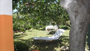 A garden with a lawn chair, a table with a tablecloth, and various plants and flowers. - Apartments Zvone (Bibinje)