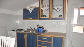 A kitchen with a central island, a stove, and a sink. There are cabinets with handles and a countertop with a knife block. - Apartments Zvone (Bibinje)