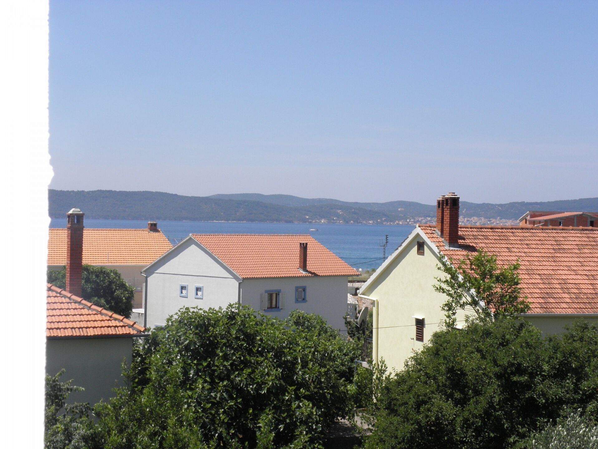 A coastal residential area with houses featuring red-tiled roofs and a clear view of the sea.