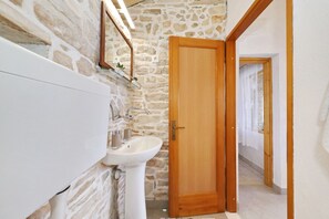 A bathroom with a stone wall, a wooden door, and a white sink. - House Doria (Vela Luka)