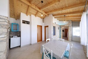 A spacious room with a wooden ceiling, stone walls, a dining table with chairs, a kitchen area with a sink, and a stone fireplace. - House Doria (Vela Luka)