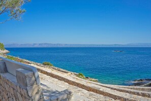 A coastal view with a stone pathway leading to the sea, clear blue water, and distant mountains. - House Doria (Vela Luka)