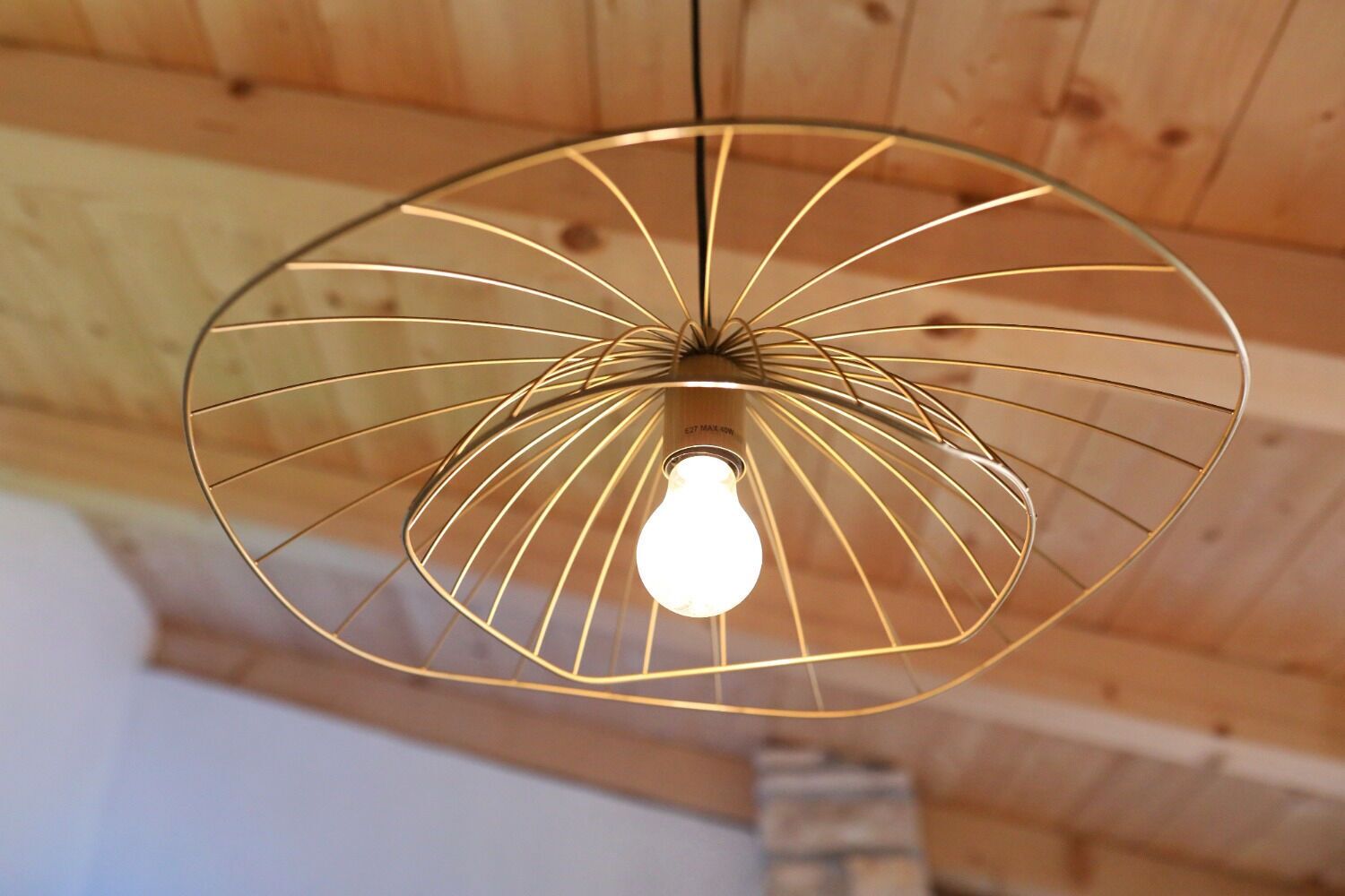 A pendant light with a geometric wire design hanging from a wooden ceiling.