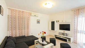 Una sala de estar con sofá, televisor y una mesita con flores.