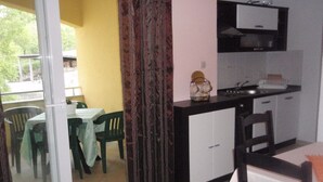 A compact kitchen with a dining area, a sliding glass door leading to an outdoor space, and a small refrigerator. - Apartment Zana (Sali)