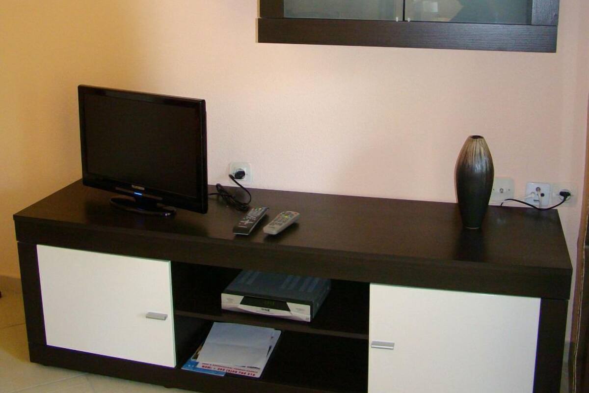 A dark wooden entertainment unit with a flat-screen TV, a remote control, and a vase.