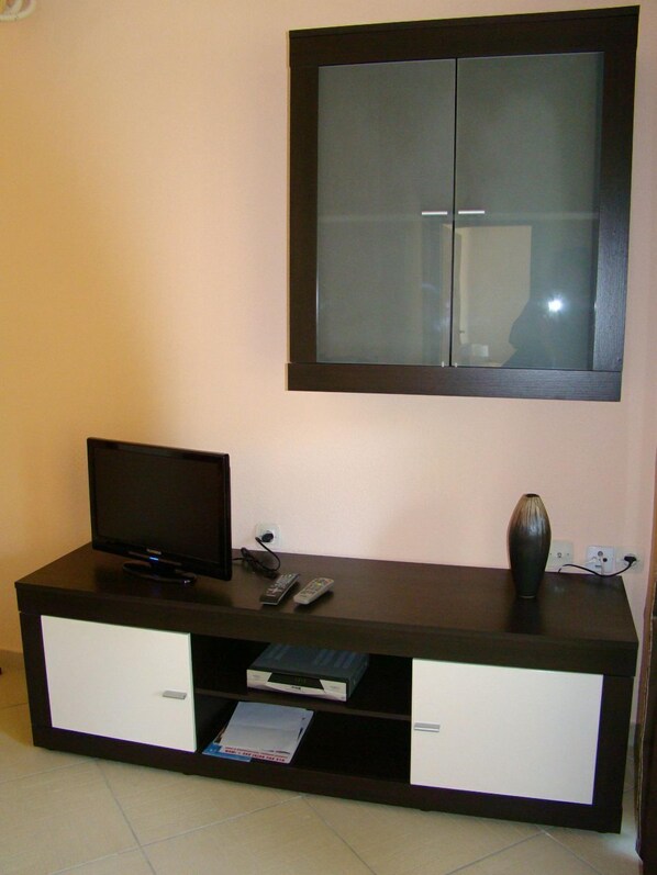 Un mueble de madera oscura para entretenimiento con un televisor de pantalla plana, un control remoto y un florero.