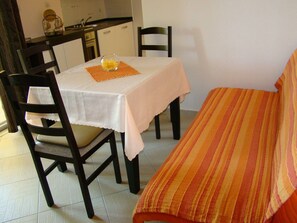 Un pequeño comedor con una mesa dispuesta para dos, una silla y una cama con manta a rayas.