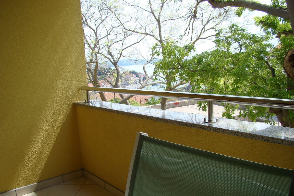 A balcony with a metal railing, a view of trees and buildings, and a yellow wall.