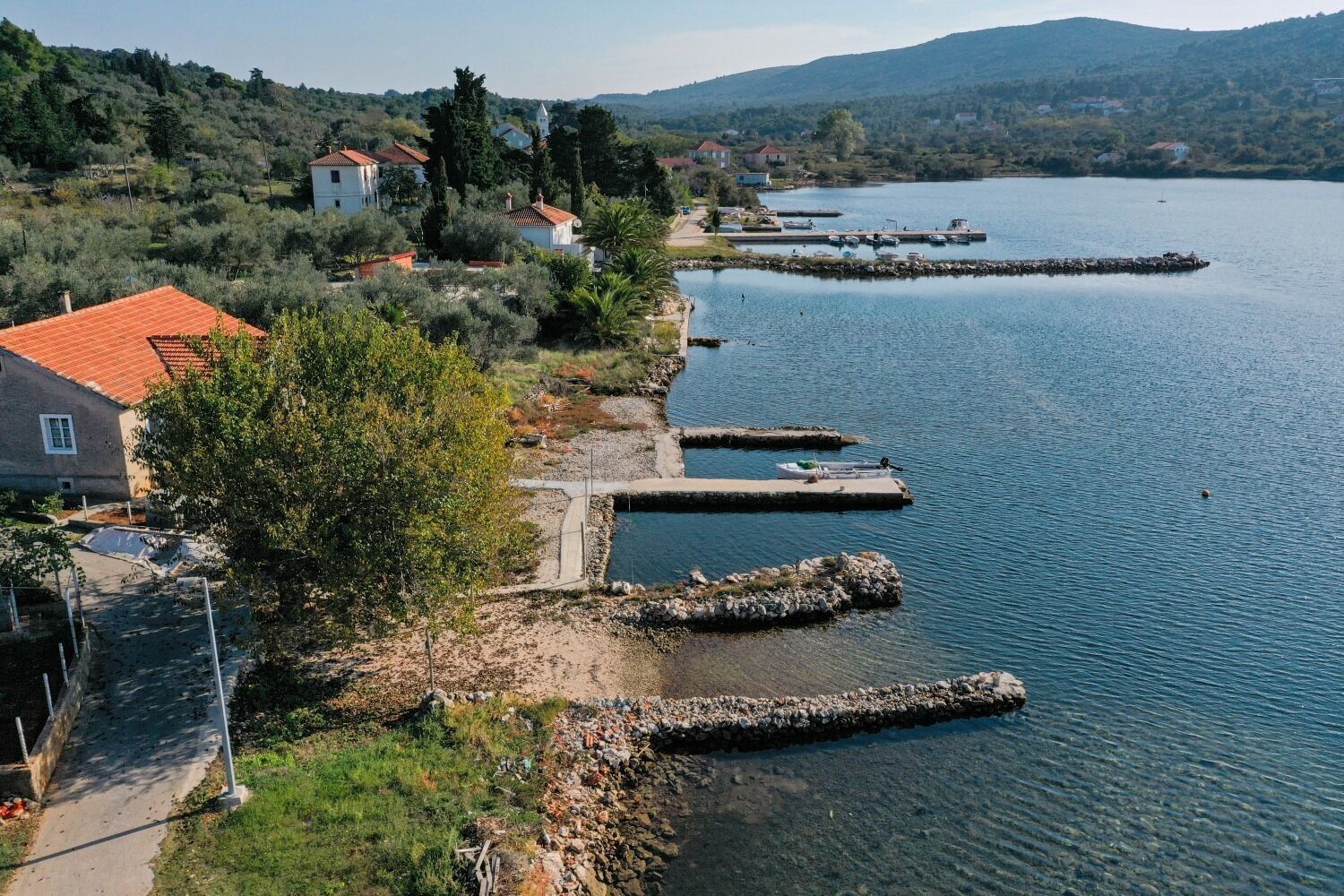 Propiedad frente al lago con muelle, camino de piedra y casas con tejas rojas.
