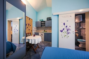 Habitación compacta con cama, una mesita y un kitchenette.