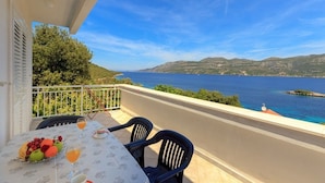 A balcony with a table set for breakfast, overlooking a body of water and hills. - Apartments Mari (Korčula)