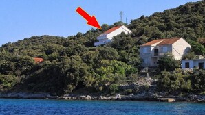 A coastal building with a red roof, surrounded by lush greenery and overlooking a body of water. - Apartments Mari (Korčula)