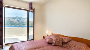 A bedroom with a bed, pillows, a nightstand, and a view of a mountainous landscape through a large window. - Apartments Mari (Korčula)