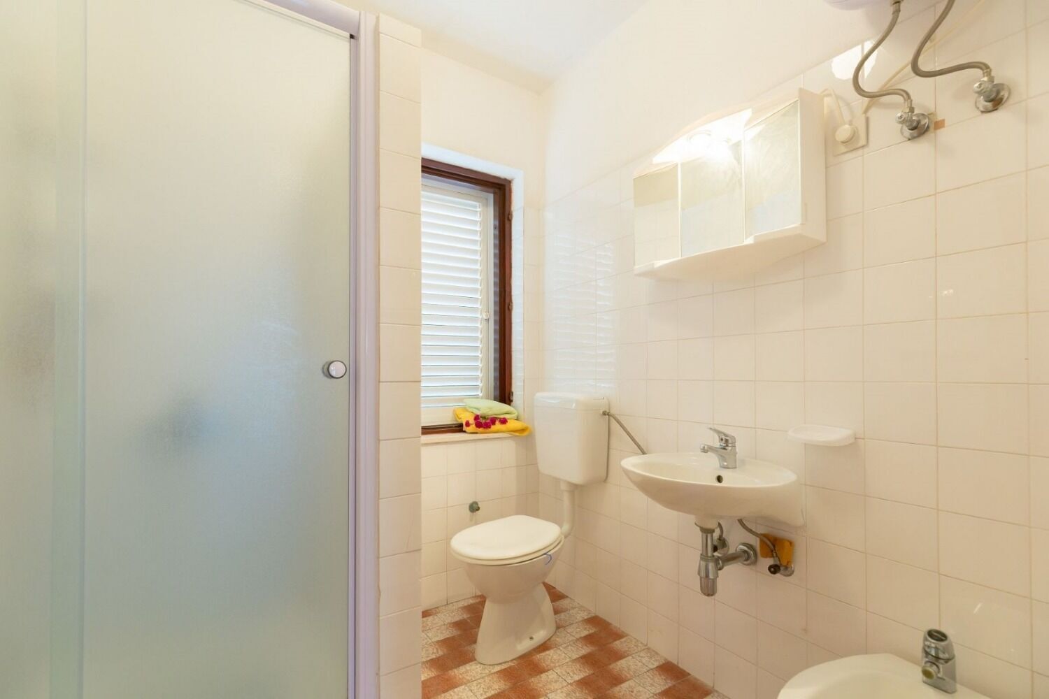 A bathroom with a toilet, sink, and window.