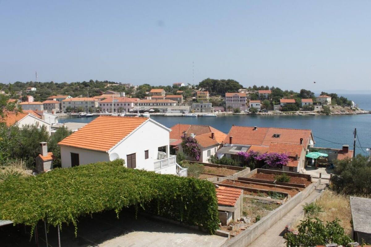 A coastal town with terracotta-roofed buildings, a marina, and a clear view of the sea.