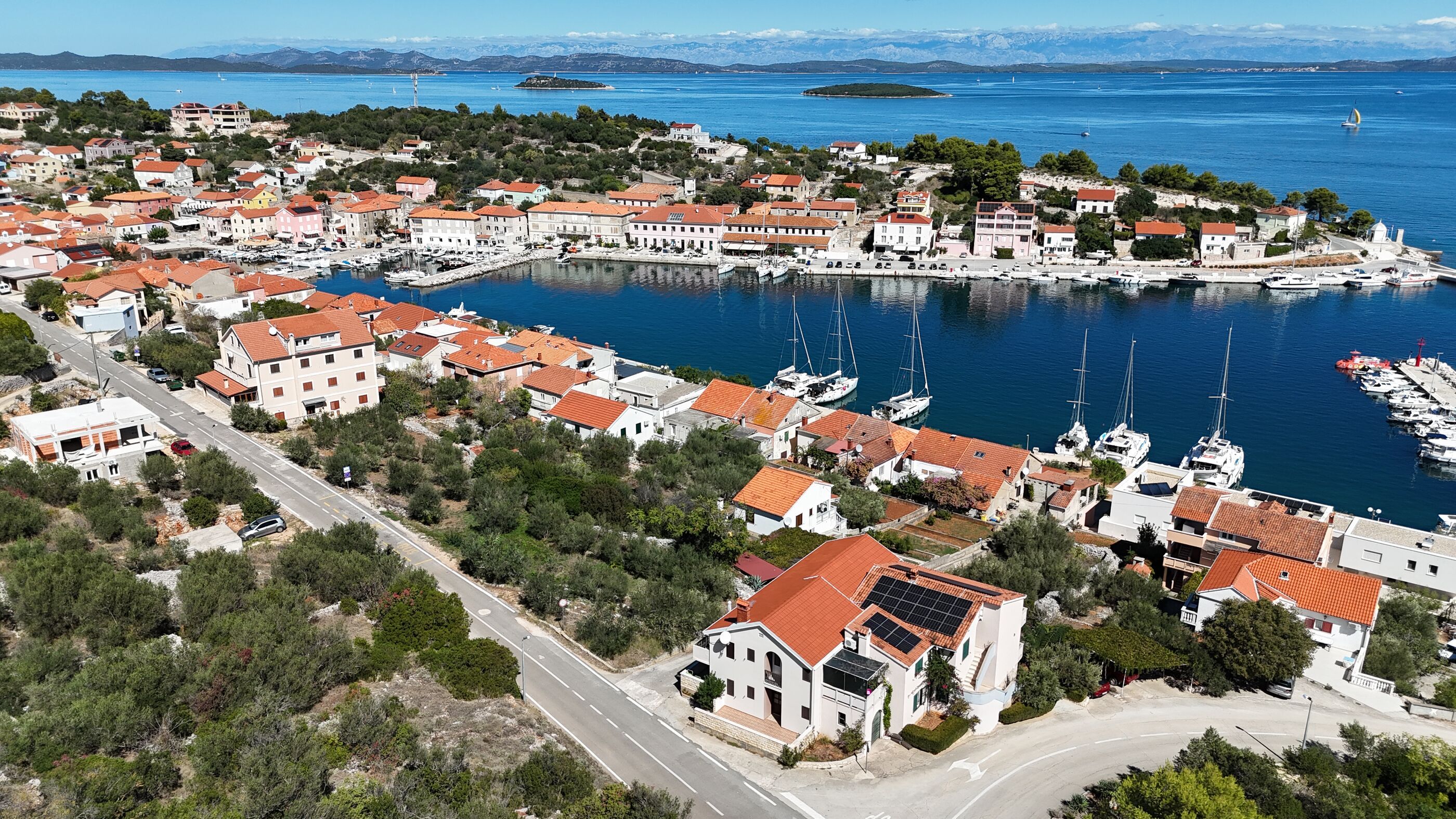 A coastal town with a marina, houses with red-tiled roofs, and a road leading into the town.