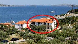 A coastal building with a red-tiled roof, surrounded by greenery and overlooking the sea. - Apartments Dari (Sali)