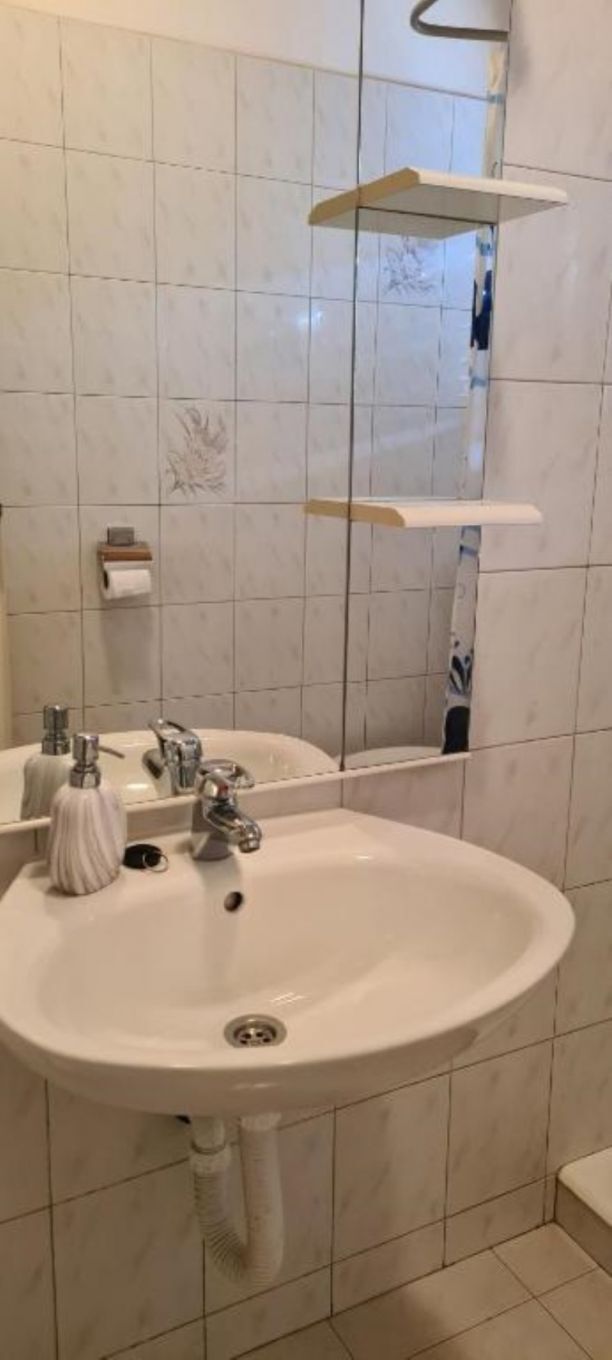 A bathroom with a white sink, two faucets, a mirror, and a towel dispenser.