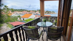 A balcony with two chairs and a table, overlooking a coastal town with buildings and a body of water. - Apartments Dari (Sali)