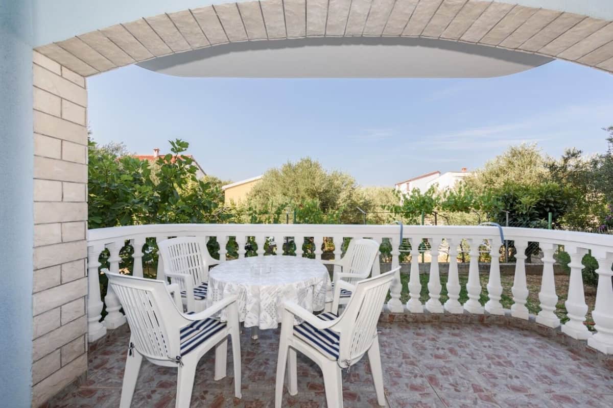 A covered outdoor seating area with a round table and white chairs, surrounded by a white balustrade.