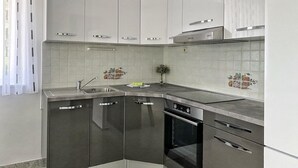 Moderni keittiö, jossa on valkoiset kaapit, ruostumattomasta teräksestä valmistettu allas ja sisäänrakennettu uuni.