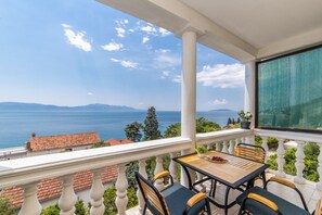 Un balcon avec une table et des chaises, offrant une vue sur la mer et les montagnes au loin.