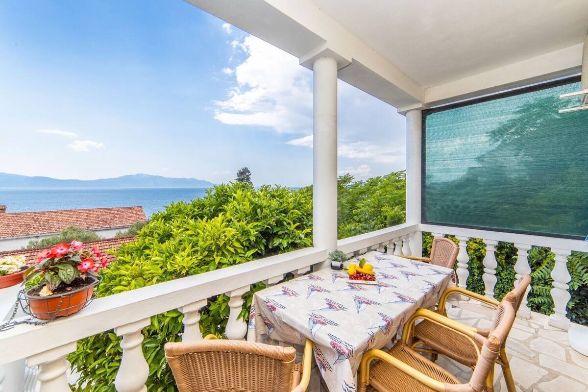 Un balcón con mesa y sillas, con vistas panorámicas al mar y las montañas.