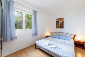 Ein Schlafzimmer mit einem Bett, zwei Nachttischlampen, einem Fenster mit Vorhängen und einem an der Wand hängenden Kunstwerk.