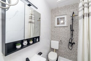 Ein Badezimmer mit Toilette, Waschbecken, Spiegel, Dusche und Fenster.