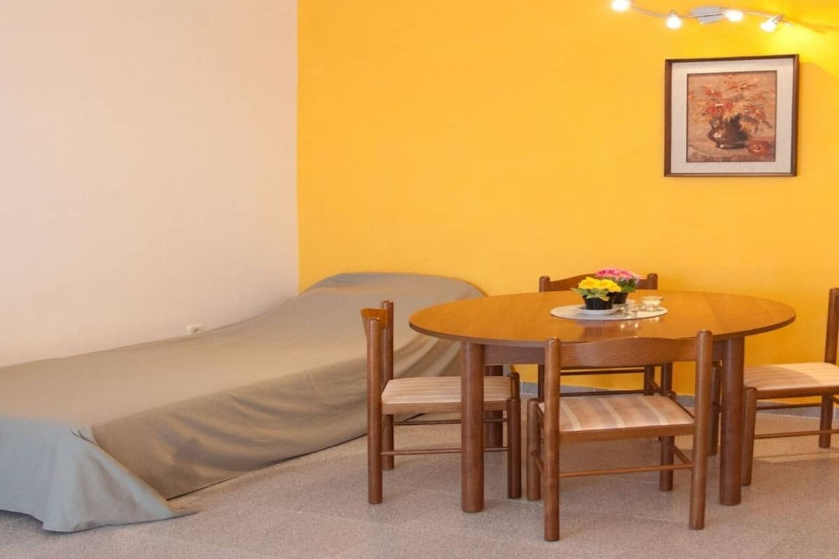 A small room with a single bed, a round wooden table with chairs, and a small table with flowers.