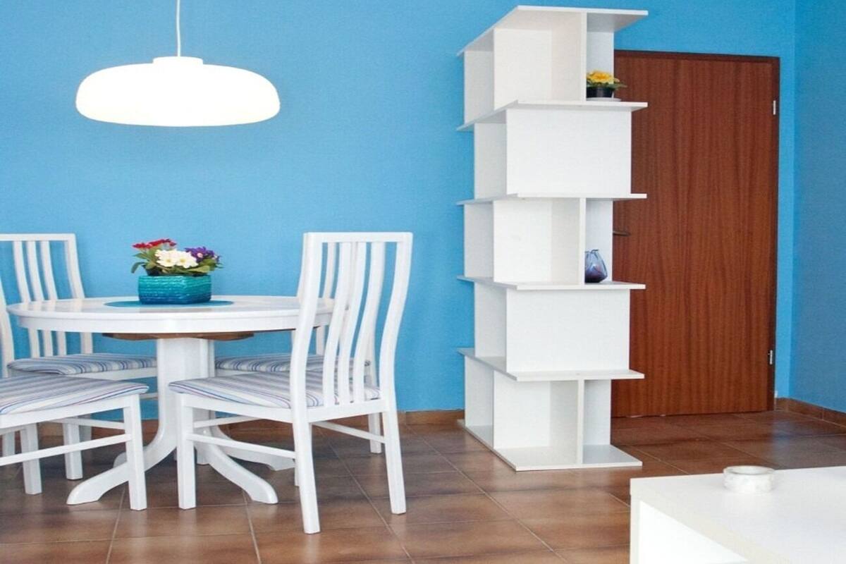 A dining area with a round table, white chairs, and a white pendant light.