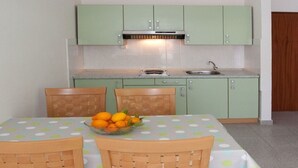 A compact kitchen with green cabinets, a dining table with a polka dot tablecloth, and a bowl of oranges on the table. - Apartments Filip (Okrug)