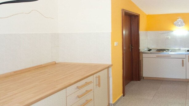 A kitchen with a wooden countertop, white cabinets, and a yellow wall. - Apartments Filip (Okrug)