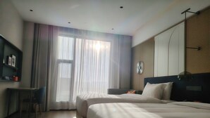 Ett hotellrum med två sängar, ett skrivbord, en TV och ett stort fönster med gardiner.