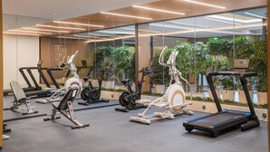 Et fitnessrum med forskellig træningsudstyr, store vinduer og indeplanter.