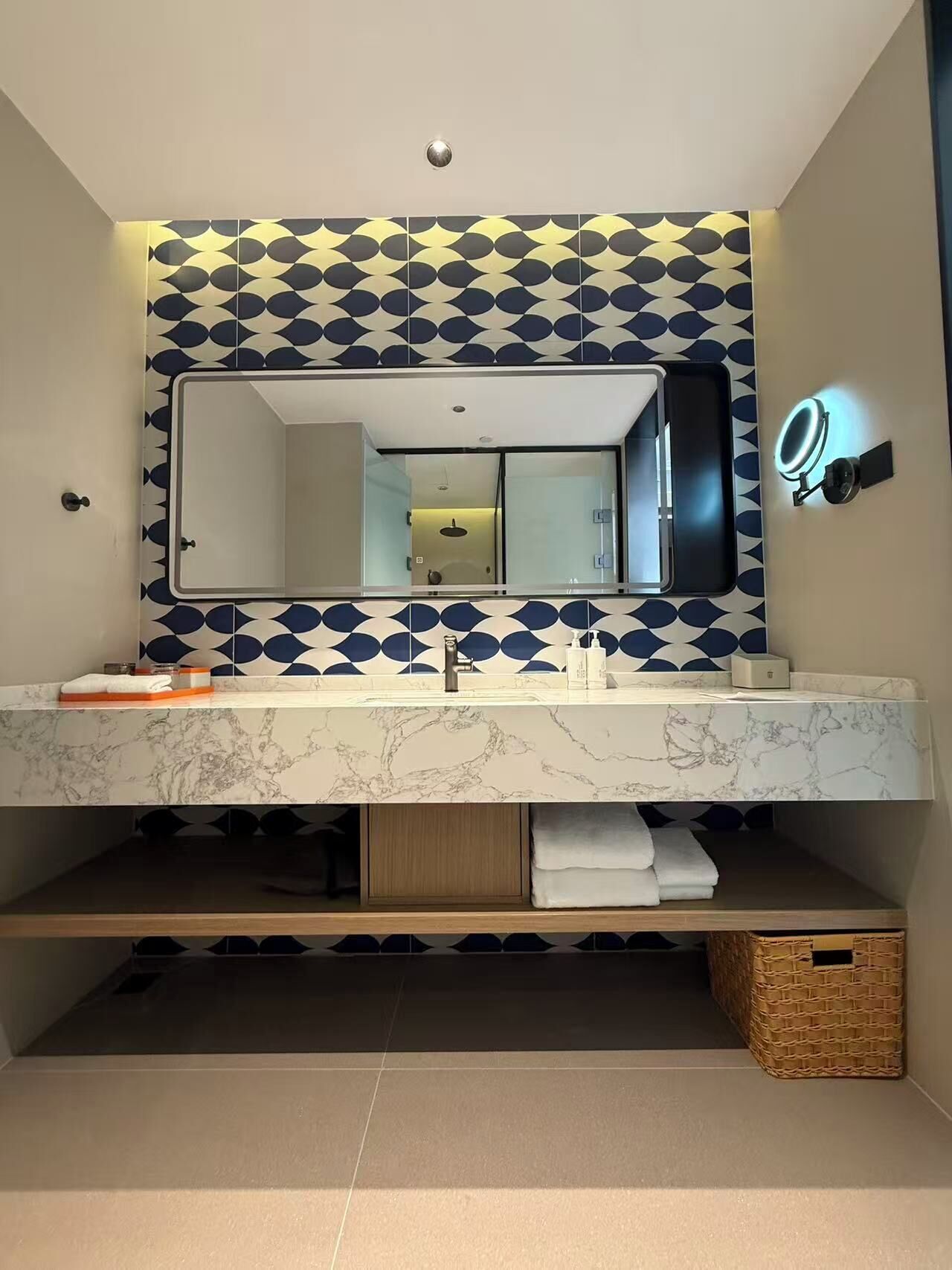 A bathroom with a large mirror, marble countertop, and a patterned wall.