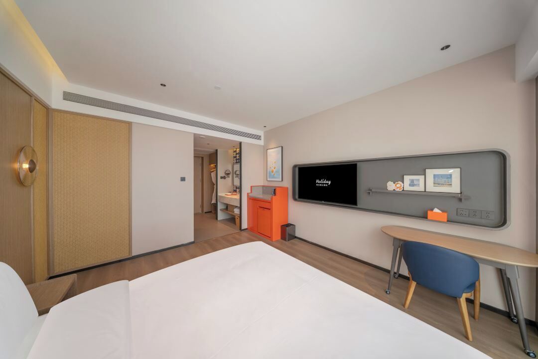 A hotel room with a bed, a desk, a television, and a bathroom visible in the background.