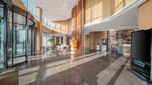 En rymlig lobby med en stor, orange maskot, en receptionsdisk och en stor skärm som visar texten ”Holiday Inn Express”.