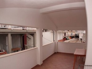 A narrow corridor with a small table and a chair, a white railing, and a view of neighboring buildings. - Apartments Marija (Hvar)