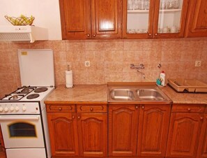 A kitchen with wooden cabinets, a stove, a sink, and a countertop. - Apartments Marija (Hvar)