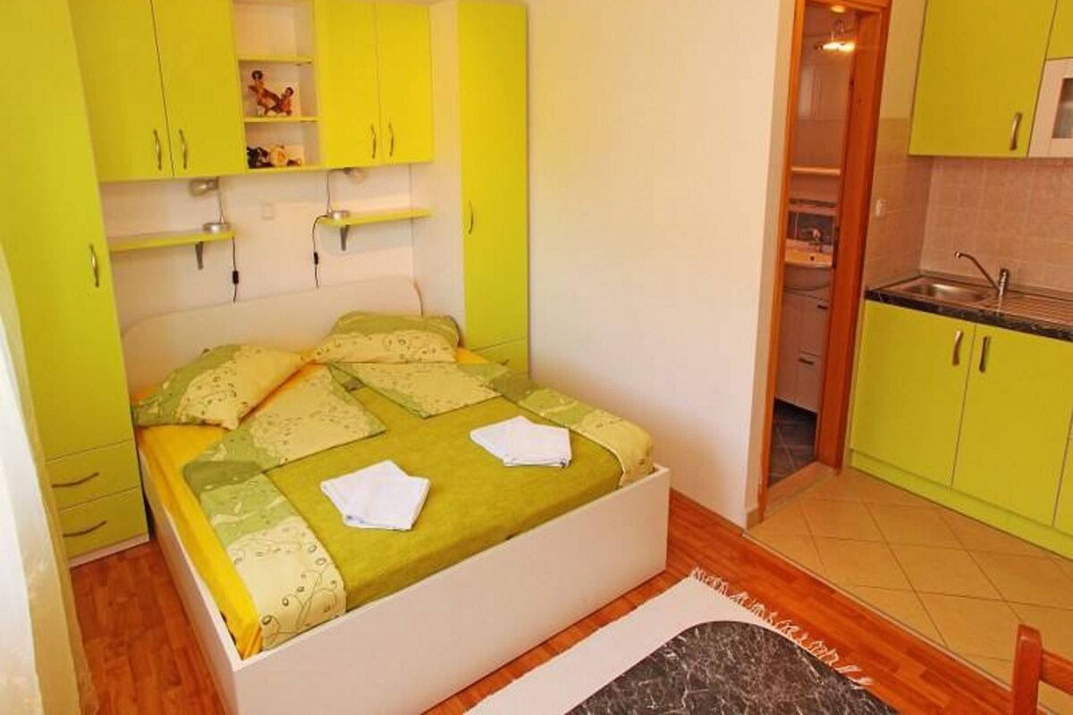 A small, bright room with a bed, a kitchenette, and a bathroom.