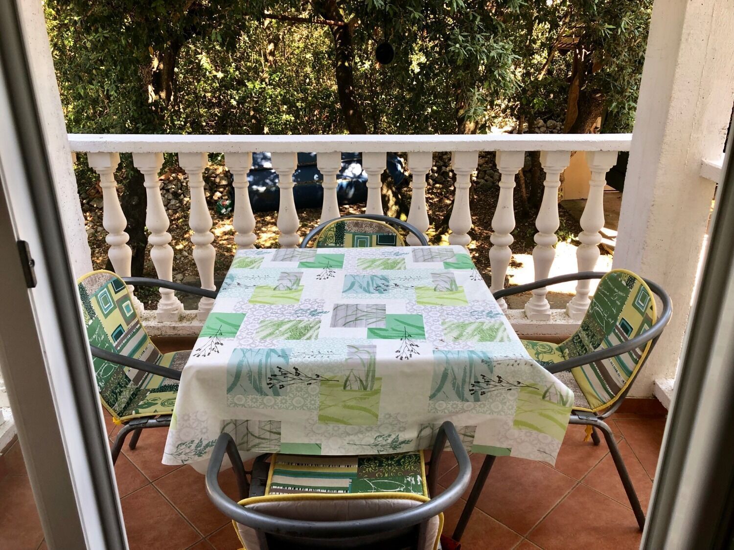 A balcony with a table covered by a quilt, two chairs with patterned cushions, and a white balustrade.