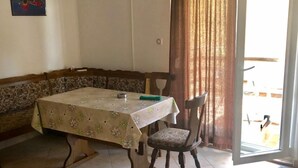 A dining area with a table covered by a floral tablecloth, two chairs, a bench, and an air conditioning unit on the wall. - Apartments Kate (Nin)