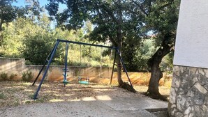 A concrete patio area with a swing set and a stone wall. - Apartments Kate (Nin)