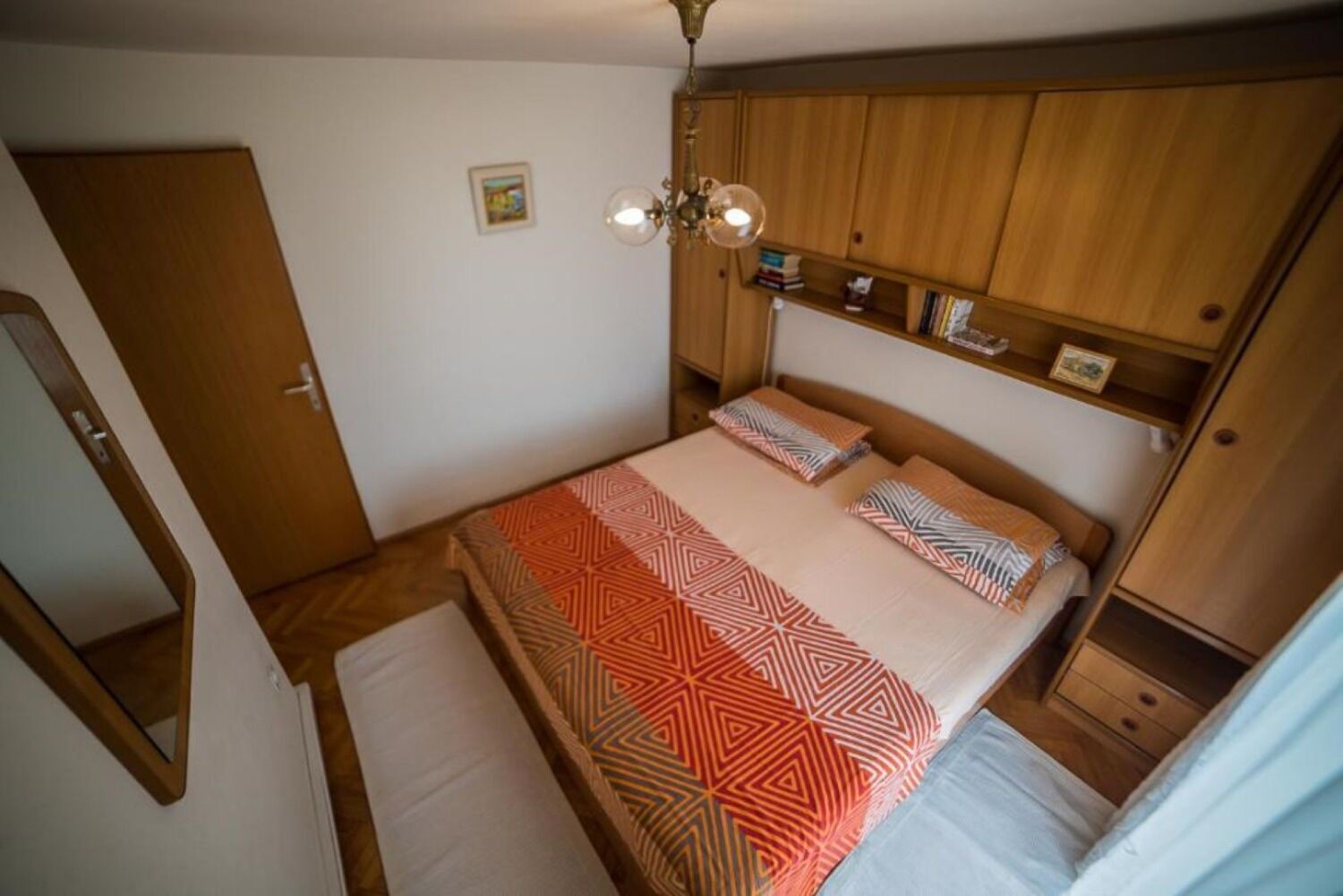 Une petite chambre à coucher, chaleureuse et accueillante, avec un lit, une armoire en bois, une table de chevet et un luminaire au plafond.