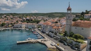 Un pueblo costero con una torre destacada, un puerto deportivo con barcos y edificios históricos con tejados de tejas rojas.