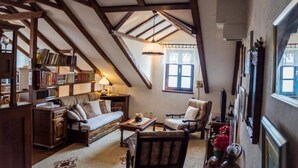 Acogedor dormitorio en ático con vigas de madera a la vista, un sofá, una silla, una mesita y una estantería llena de libros.