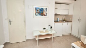 A compact kitchen with white cabinets, a small table with a glass top, and a painting on the wall. - Apartments Sea Front (Slivno)